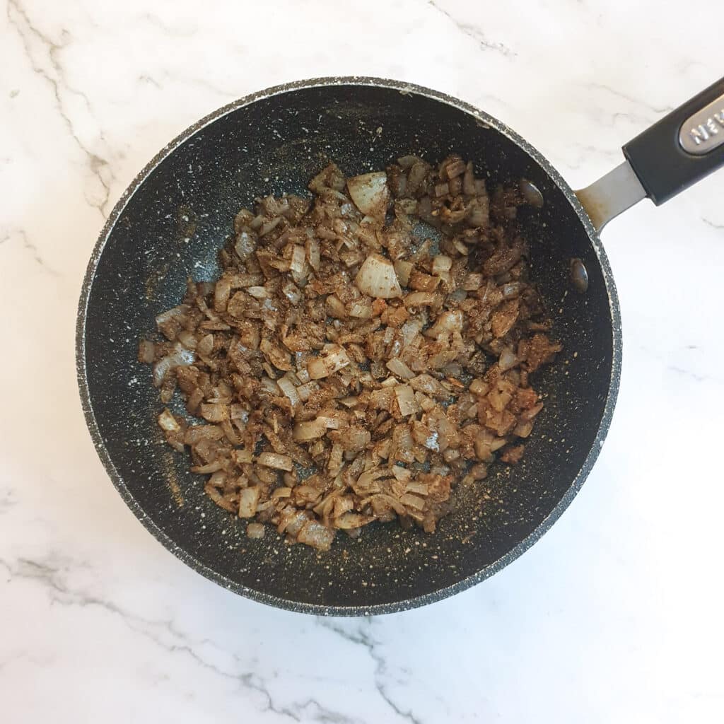 Spices added to onions in a frying pan.