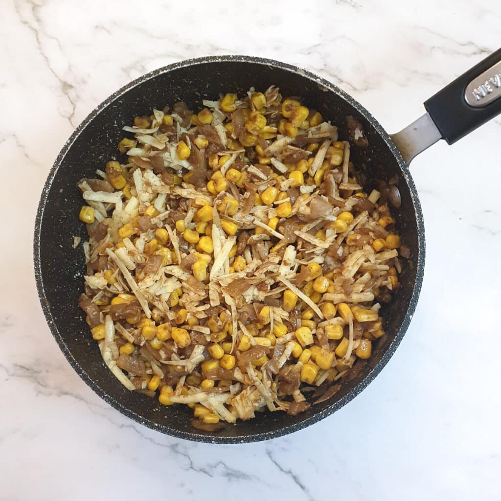 Grated cheese mixed into the cooled sweetcorn filling in a frying pan.