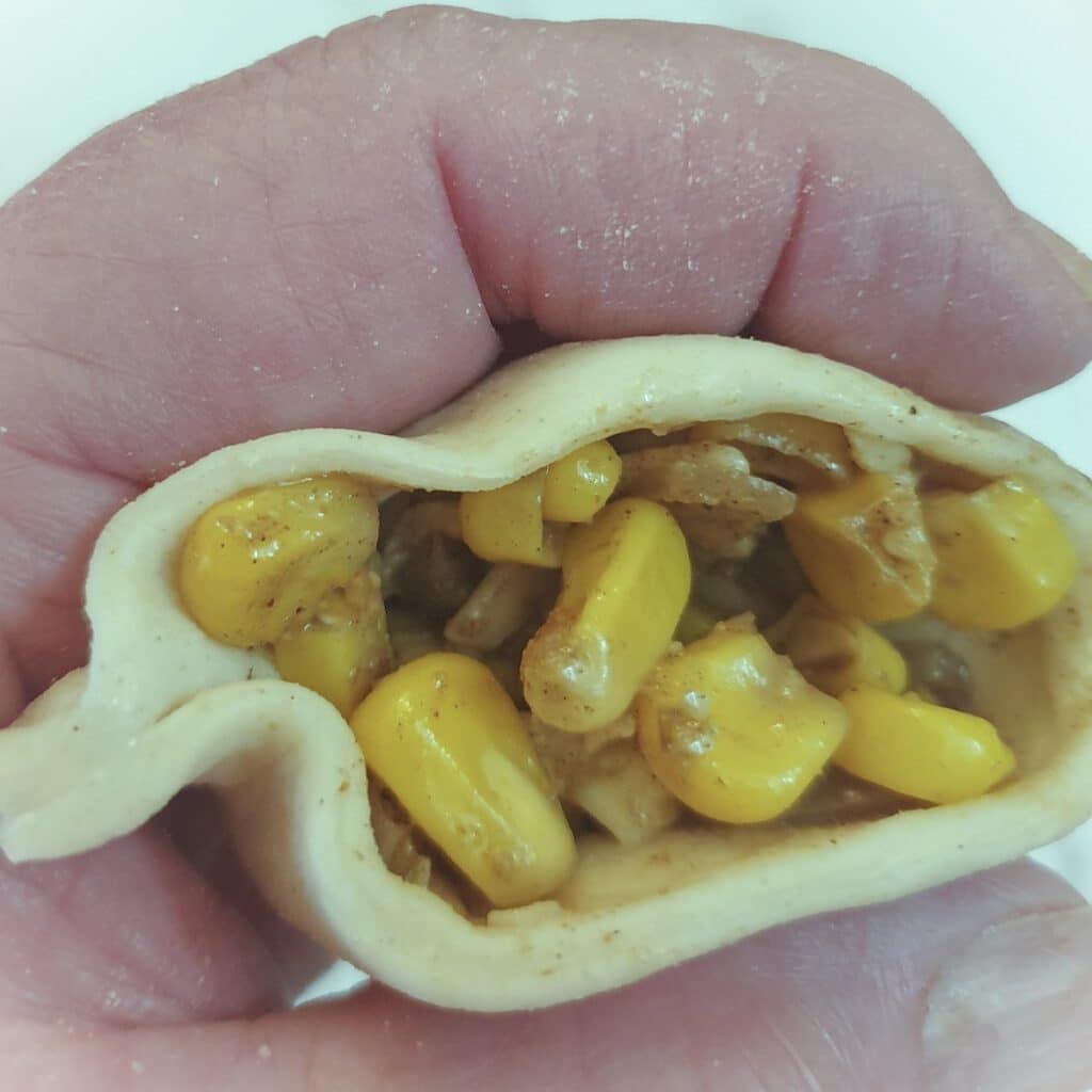 Cheese and sweetcorn filling being spooned into a pastry shell.