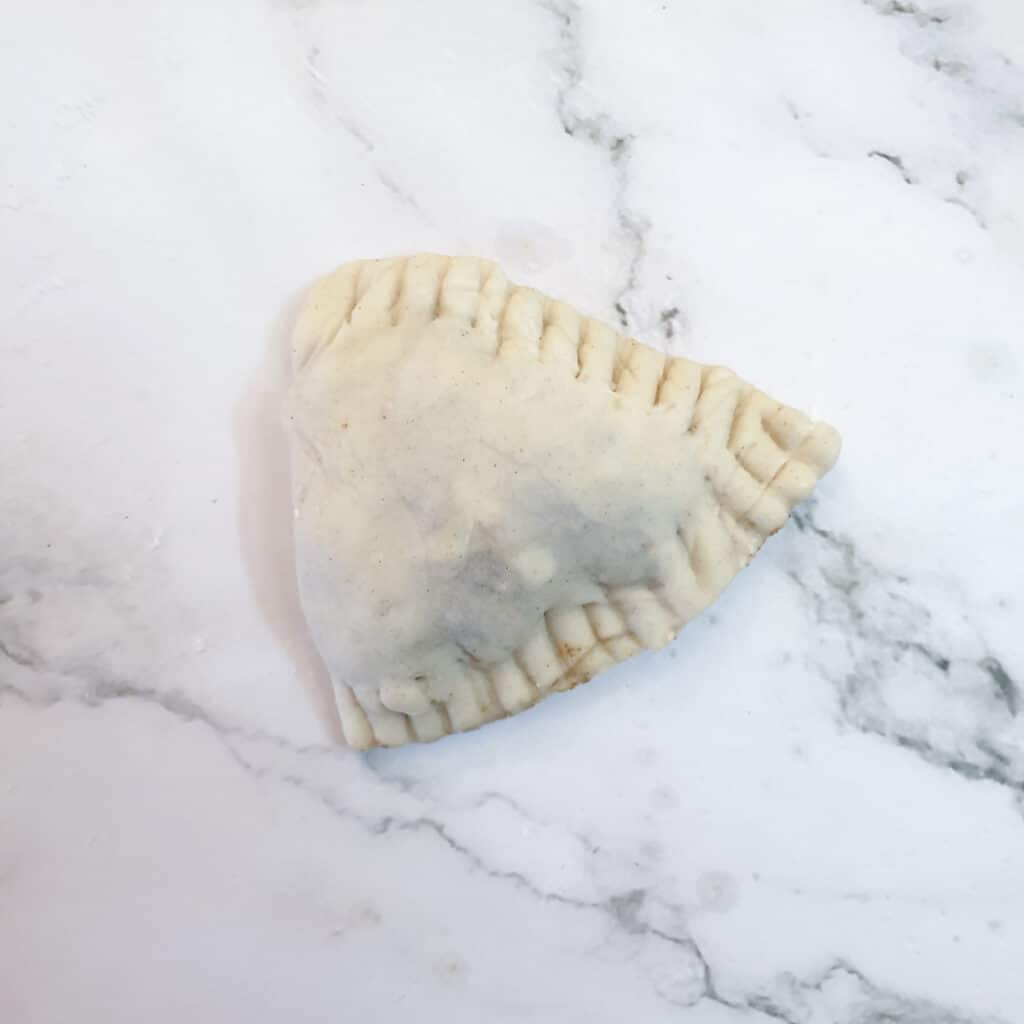 An unbaked cheese and sweetcorn samosa showing the crimped edges.