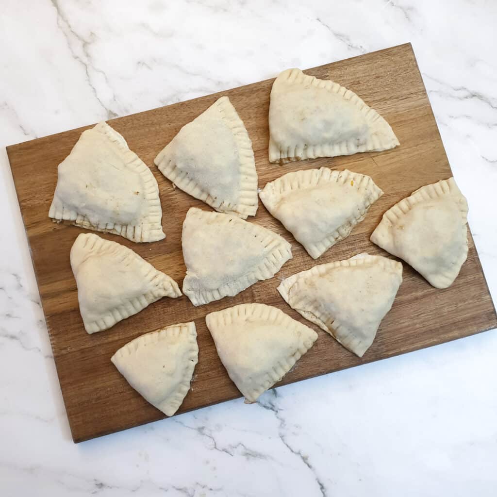 10 unbaked samosas on a wooden board.