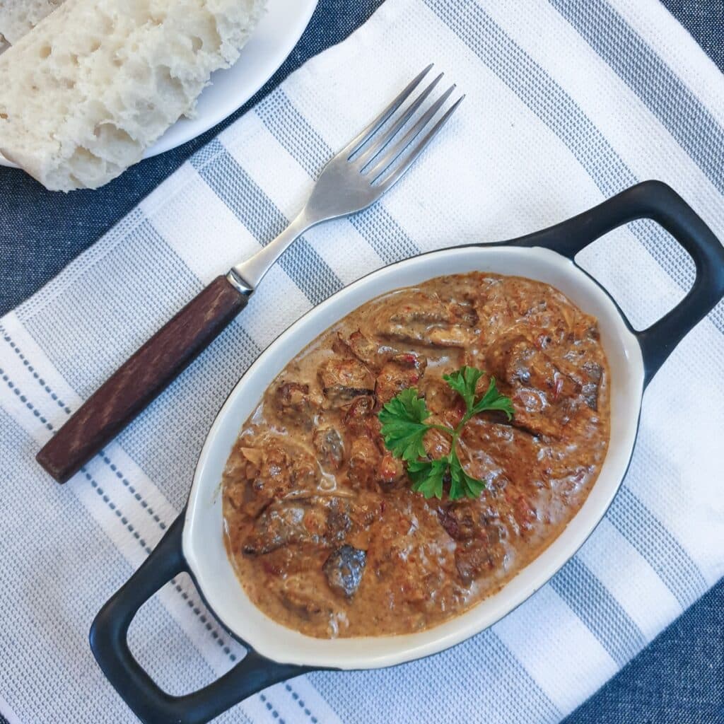 A dish of chicken livers in creamy red pepper sauce, on a blue and white striped placemat. A dish of chicken livers in creamy red pepper sauce, on a blue and white striped placemat.