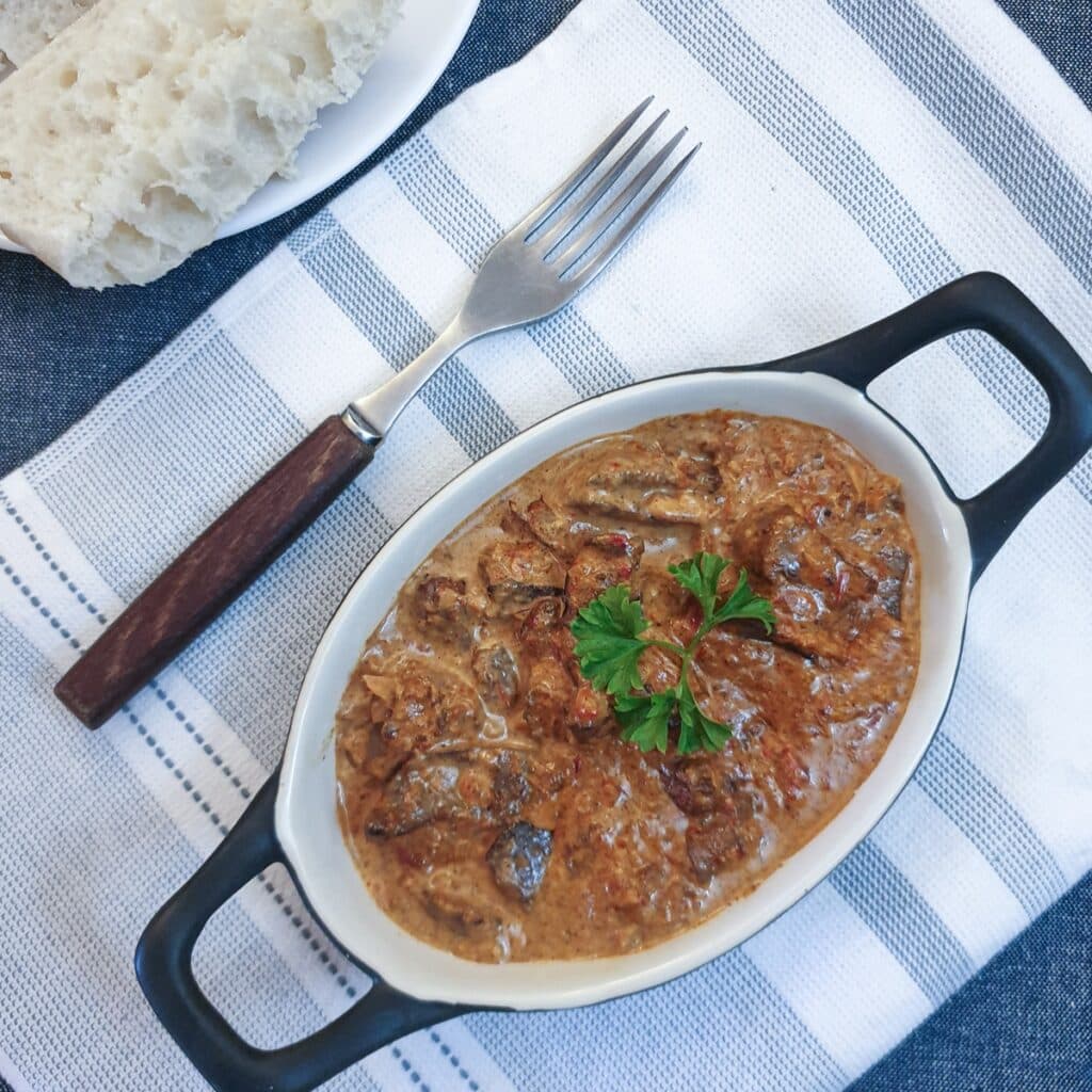 A dish of chicken livers in creamy red pepper sauce, on a blue and white striped placemat.