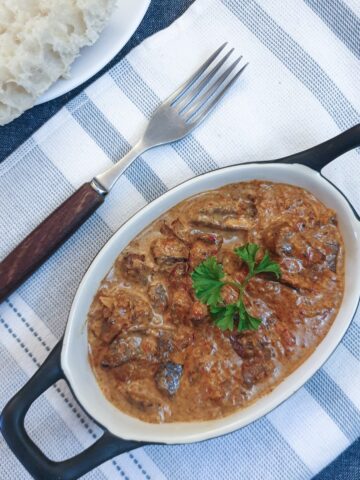 A dish of chicken livers in creamy red pepper sauce, on a blue and white striped placemat.