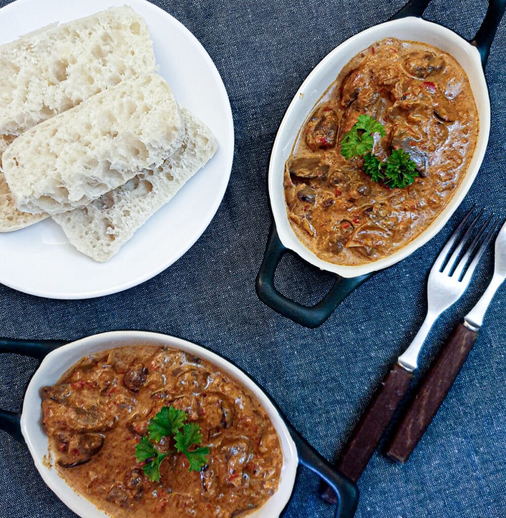 Two small dishes of chicken livers alongside a plate of crusty bread.