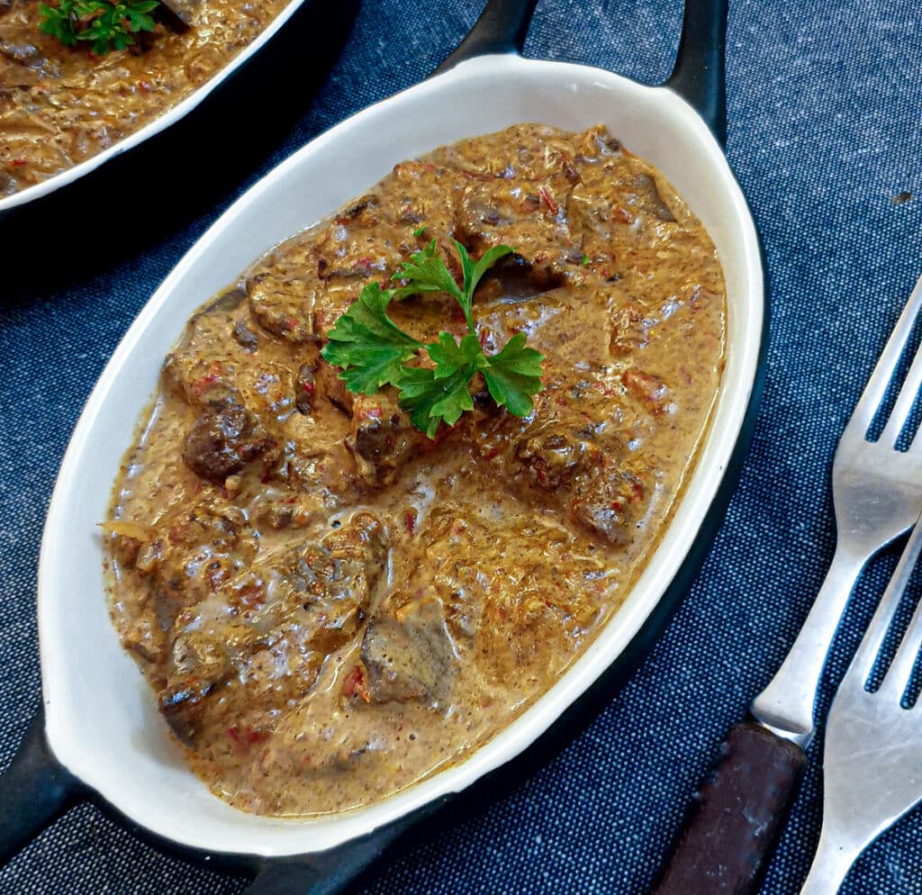 Overhead shot of creamy red pepper chicken livers in a white dish on a blue background.