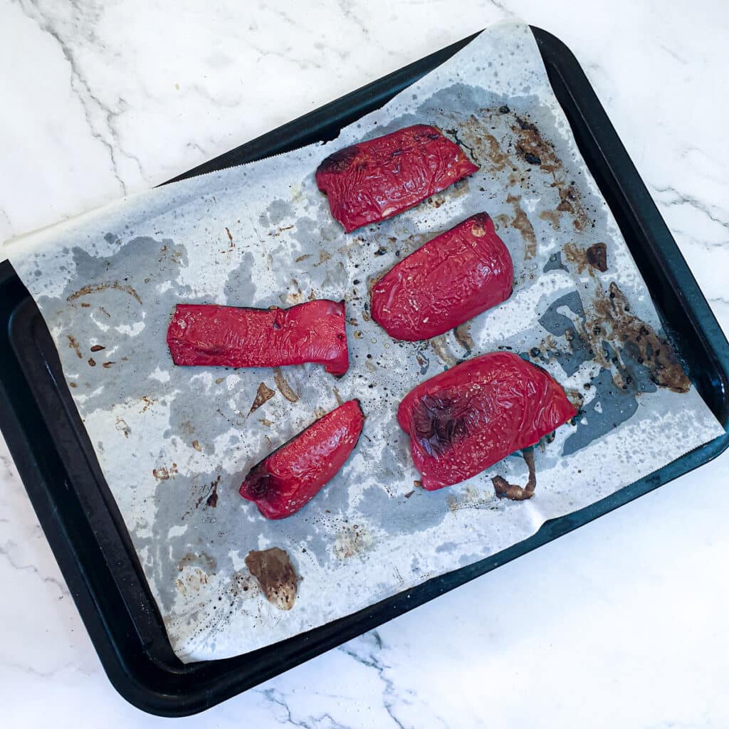 Red peppers on a baking tray having been left in the oven for an extra few minutes to develop a 'char'.