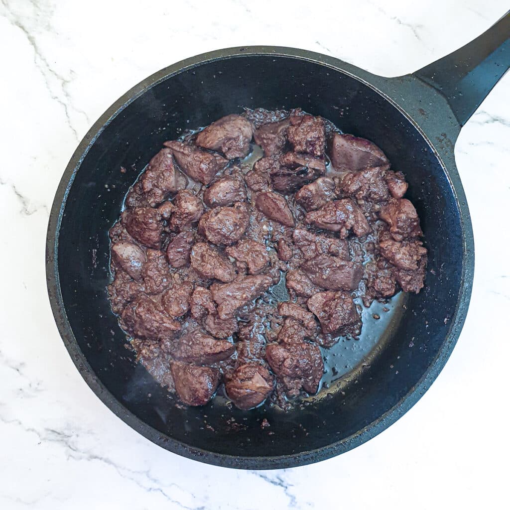 Chicken livers being browned in butter and oil in a frying pan.