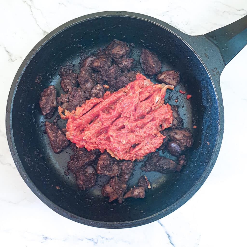 Blended red peppers and onions added to chicken livers in a frying pan.