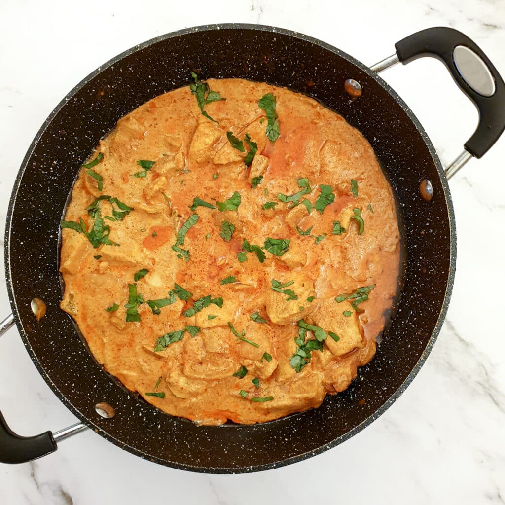 A frying pan of butter chicken garnished with chopped coriander.