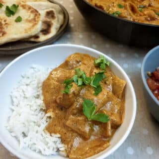 A serving of butter chicken on rice in a white dish.
