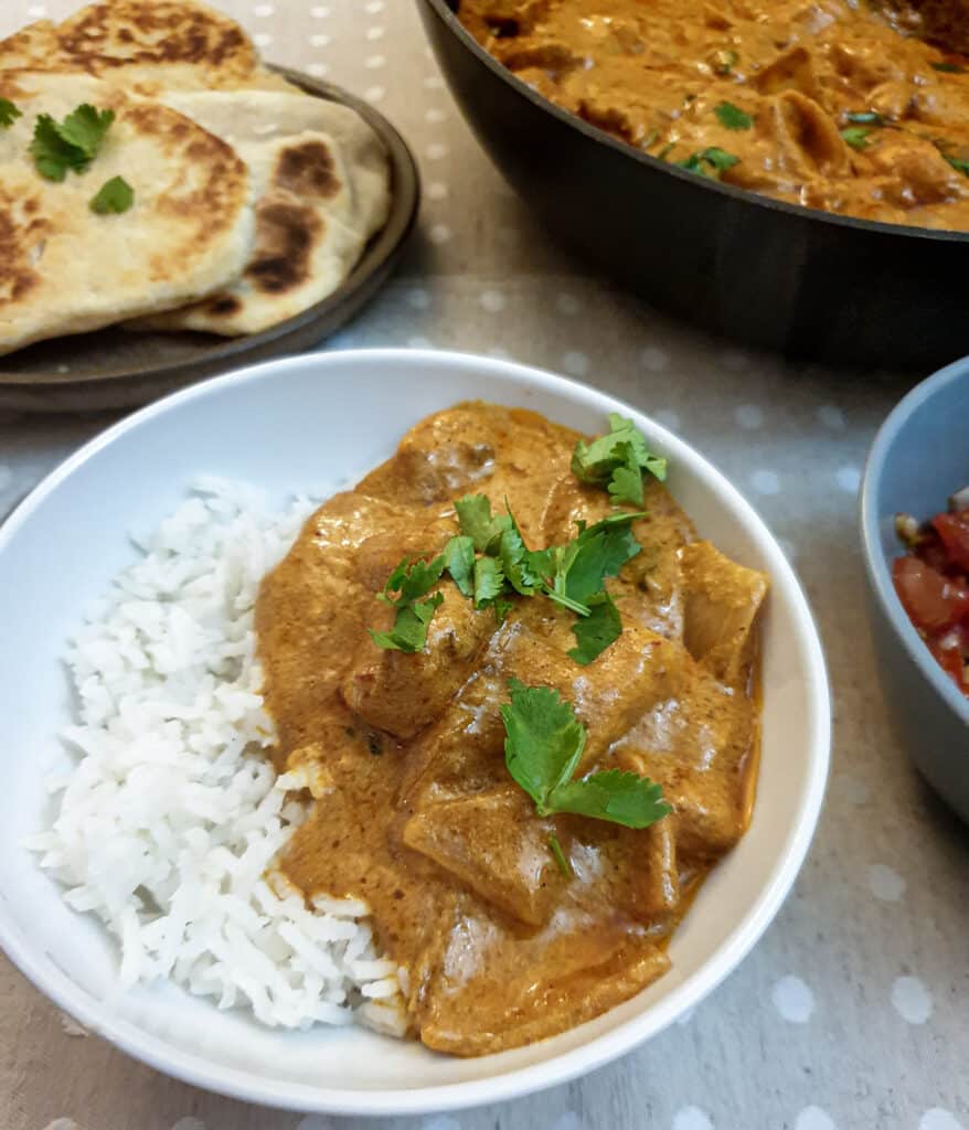 A serving of butter chicken on rice in a white dish.