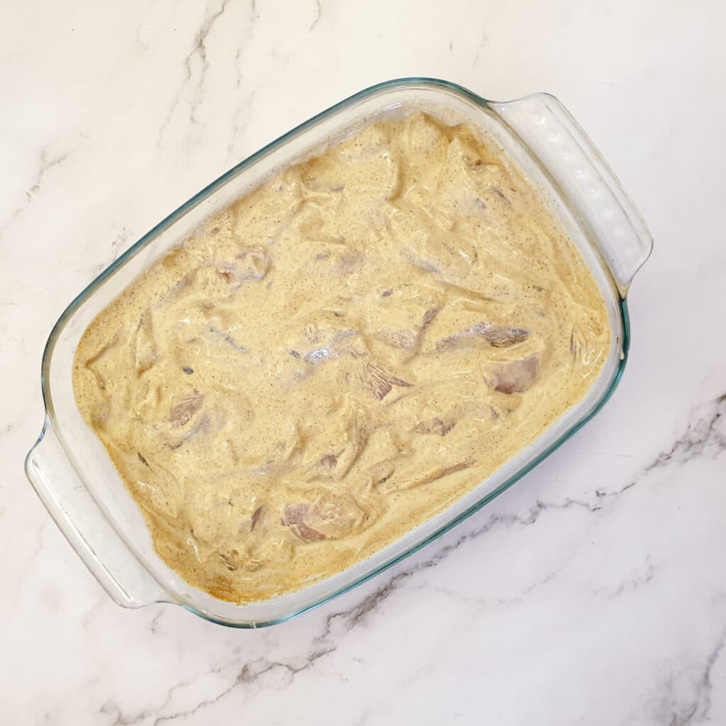 A glass dish filled with chicken pieces marinating in a butter curry sauce.