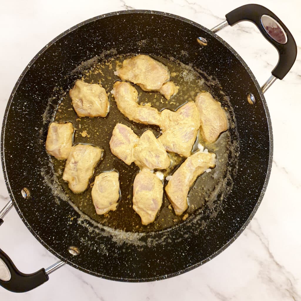 Pieces of chicken being fried in a frying pan.