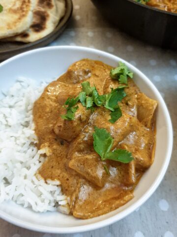 A serving of butter chicken on rice in a white dish.