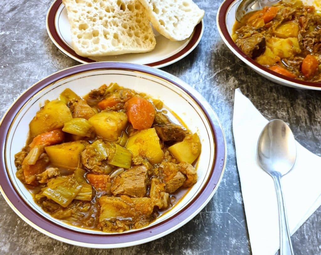 A plate of lamb stew on a table next to a spoon on a serviette.