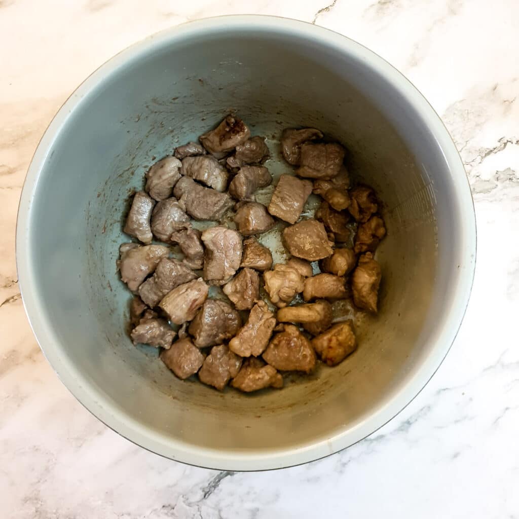 Pieces of lamb browning in the inner pot of a Ninja pressure cooker.