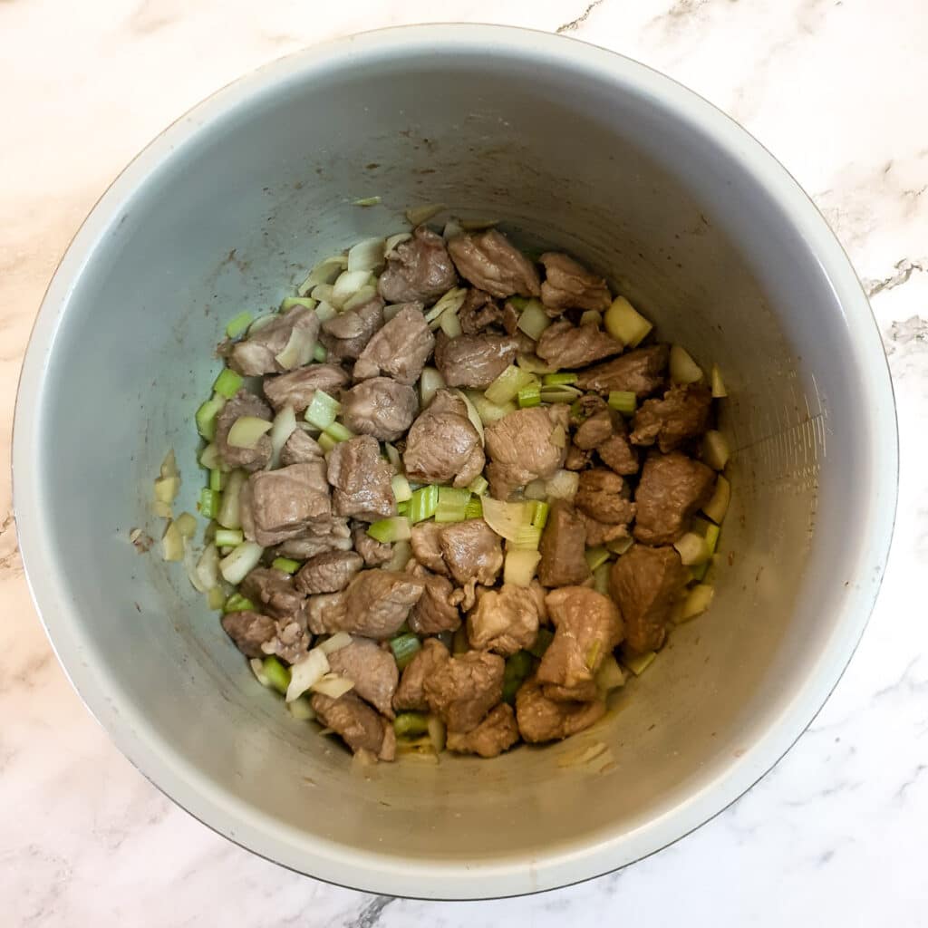 Browned lamb with onions and celery in a pressure cooker.