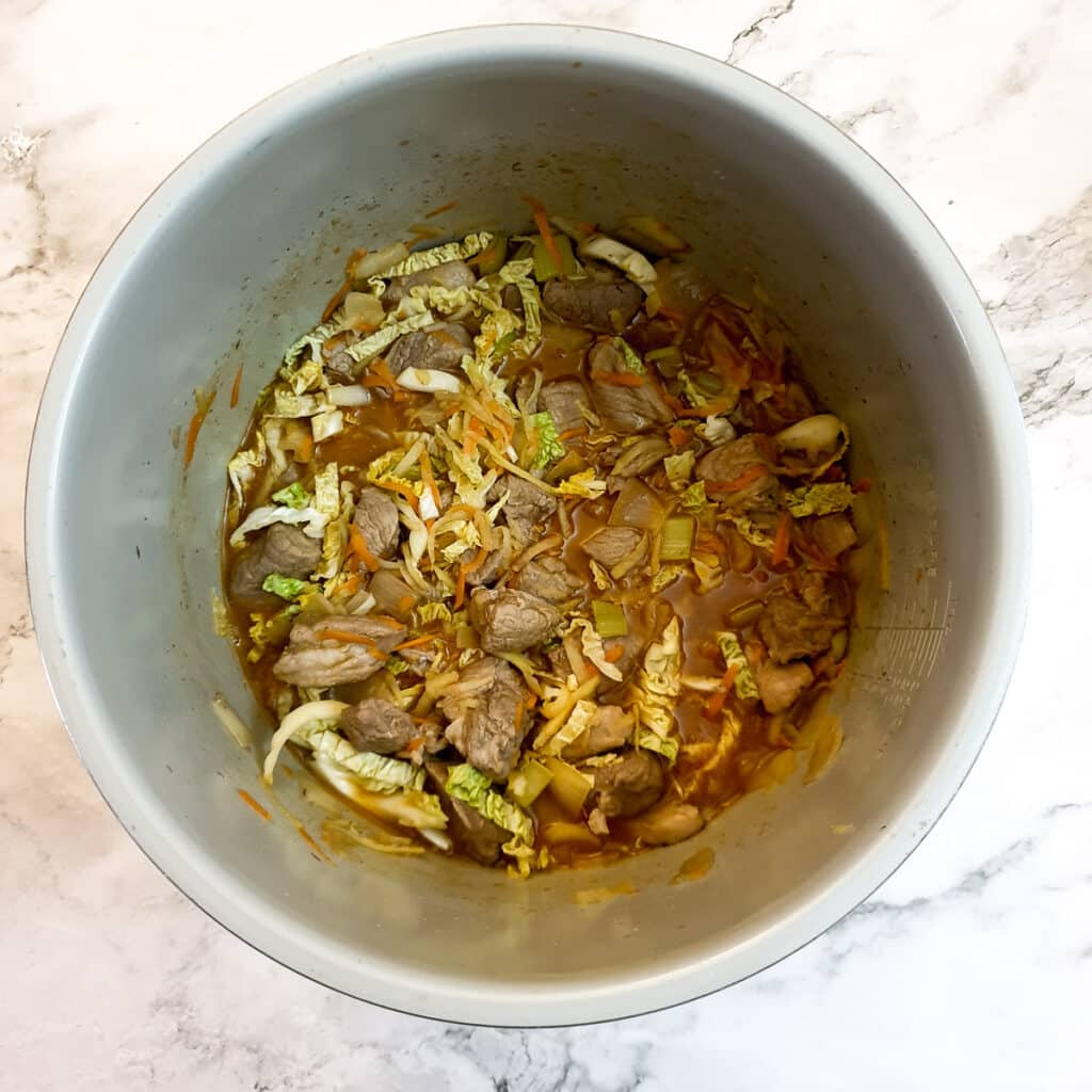 Stock and grated vegetables in a pressure cooker with pieces of lamb.