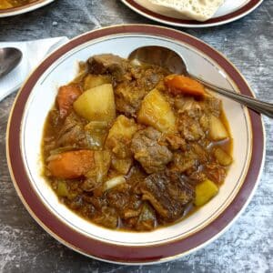 A plate of lamb stew in a red-rimned dish with a spoon.