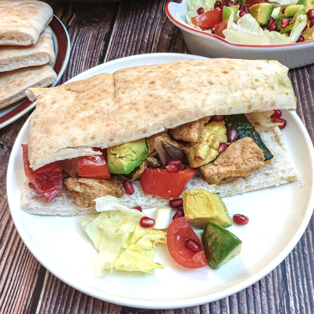 A pita bread stuffed with Moroccan chicken and vegtables on a white plate.