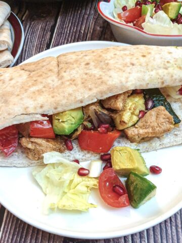 A pita bread stuffed with Moroccan chicken and vegtables on a white plate.