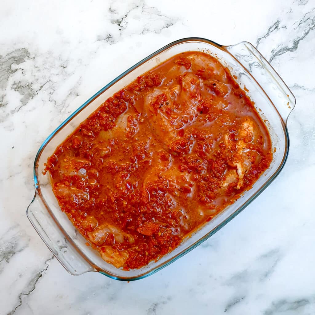 Peri peri chicken in a glass bowl, covered with marinade.