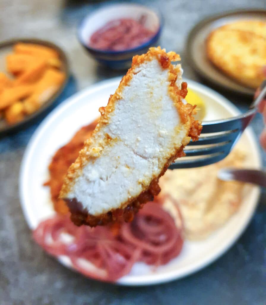 A piece of peri peri chicken on a fork with out-of-focus dishes in the background.