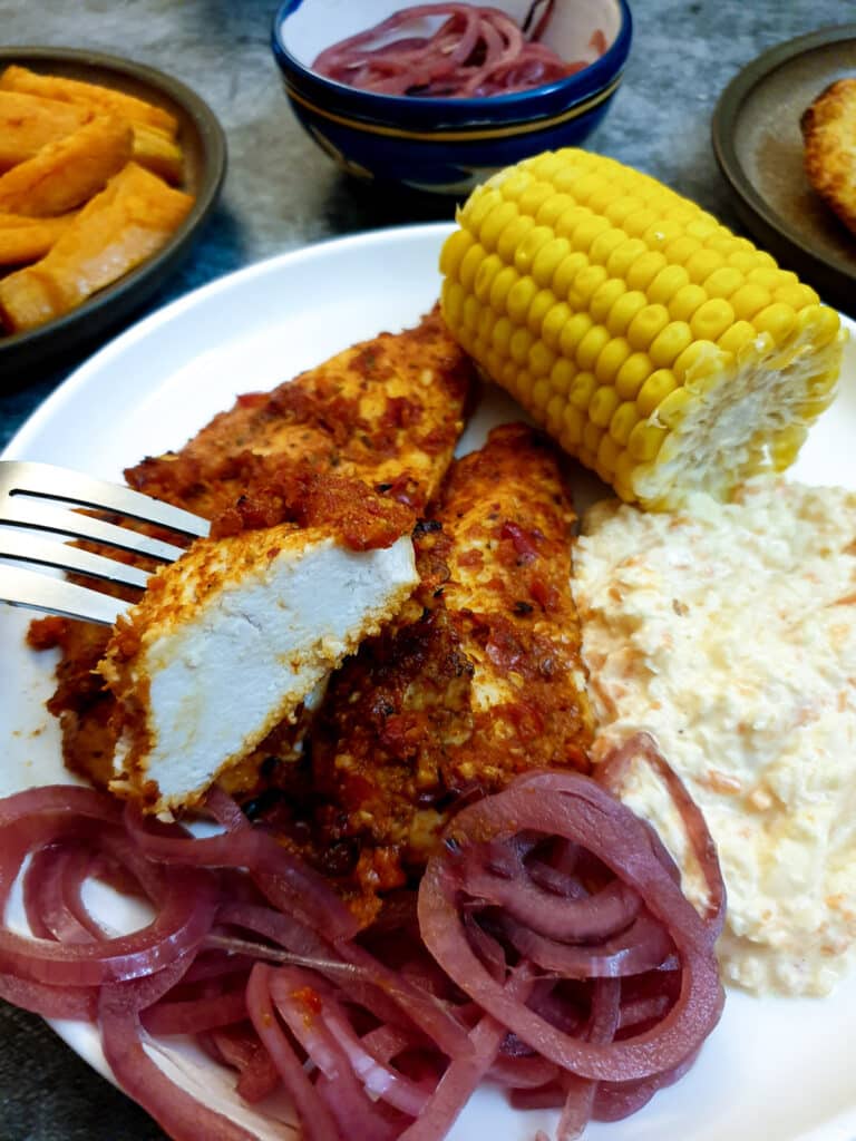 A piece of peri peri chicken with a cob of sweetcorn in the background. 