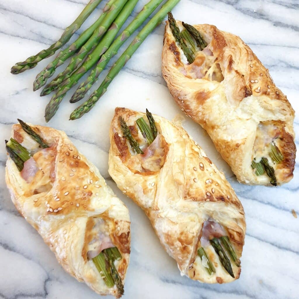 3 ham and asparagus wraps on a marble board with spears of fresh asparagus at the side.