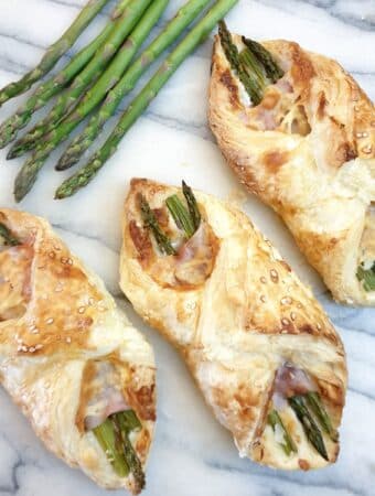 3 ham and asparagus wraps on a marble board with spears of fresh asparagus at the side.