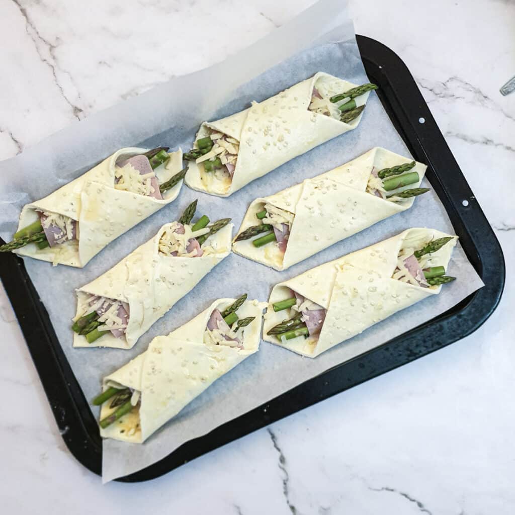 6 puff pastry asparagus and ham wraps on a baking tray.