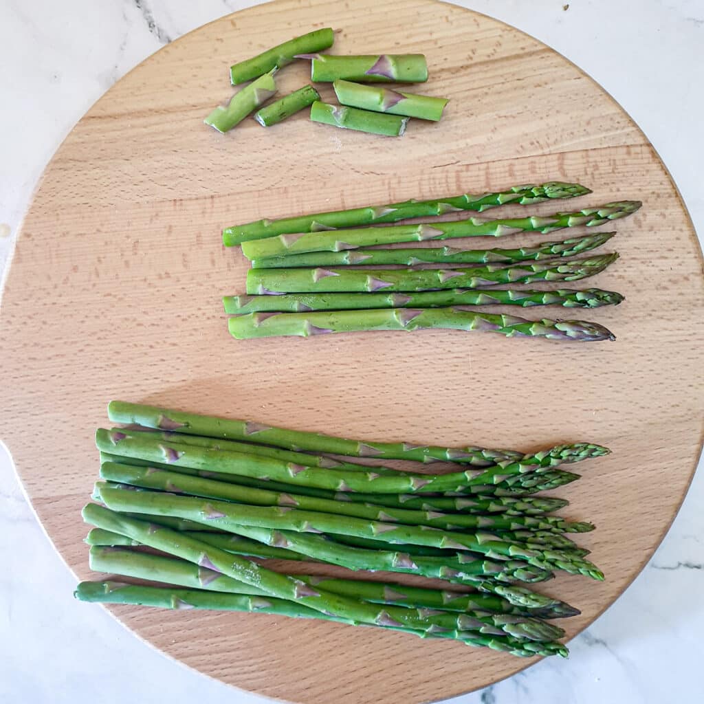 Asparagus spears on a wooden board showing the ends snapped off.