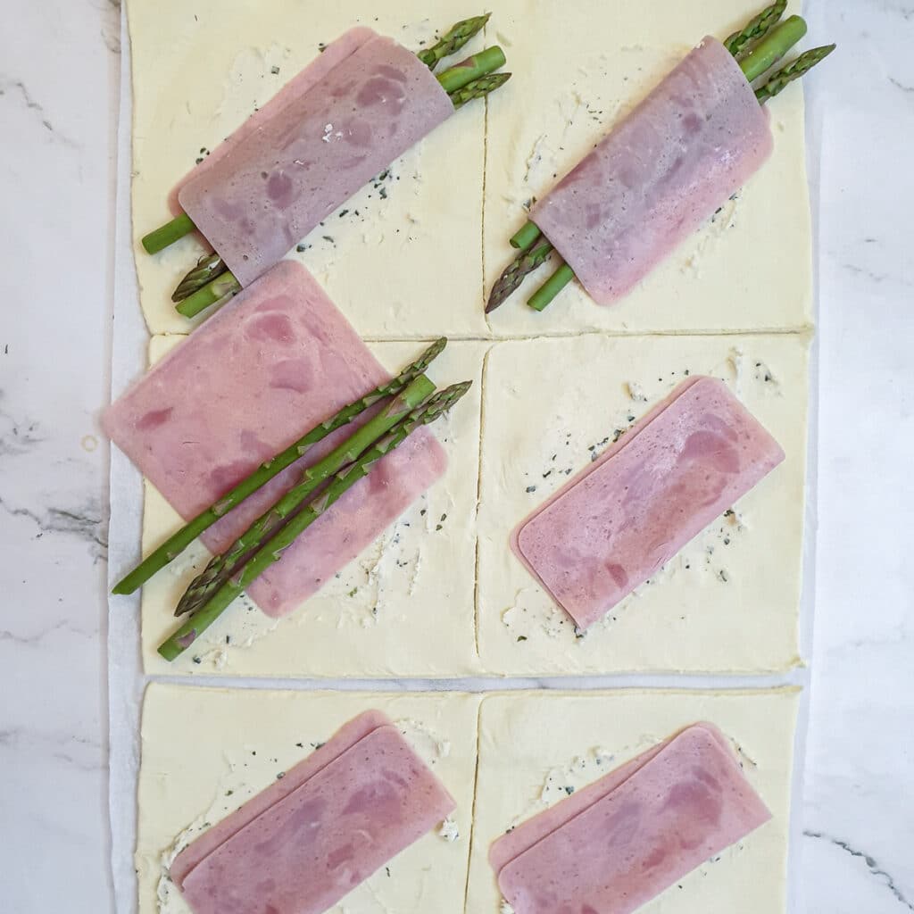 Asparagus spears being added to the ham on the puff pastry squares.