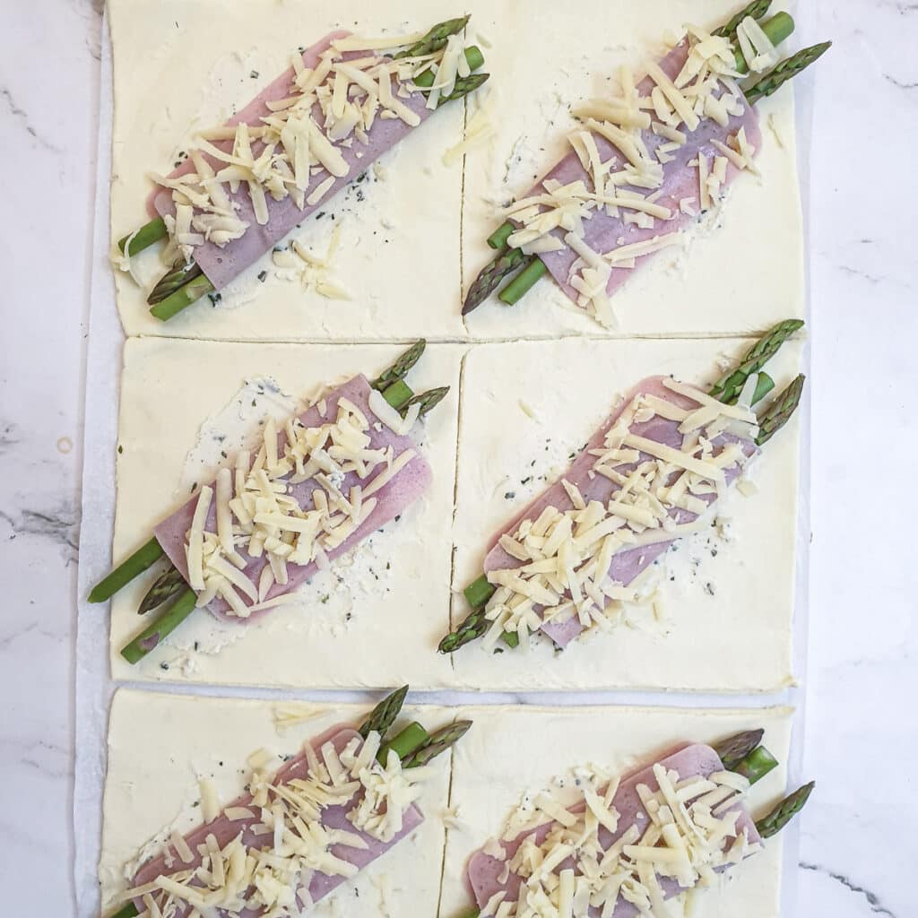 Grated cheese sprinkled over the ham and asparagus on the puff pastry squares.