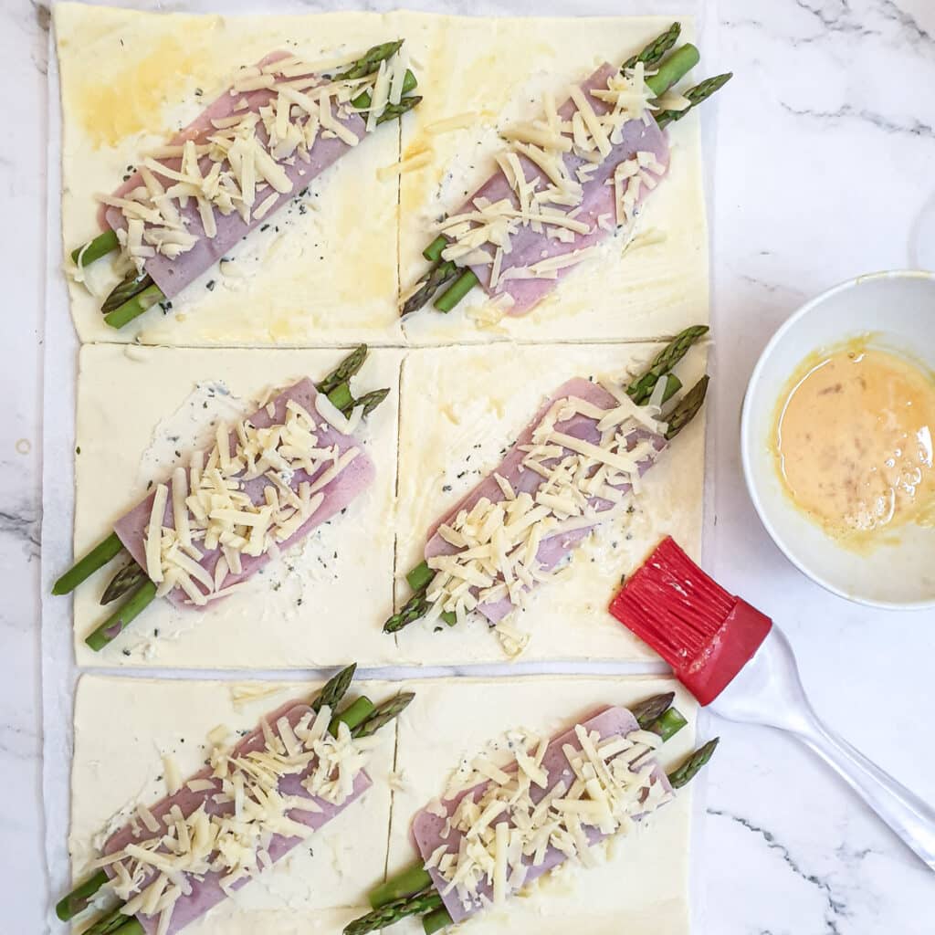 Beaten egg being brushed onto the corners of the ham and asparagus pastry squares.