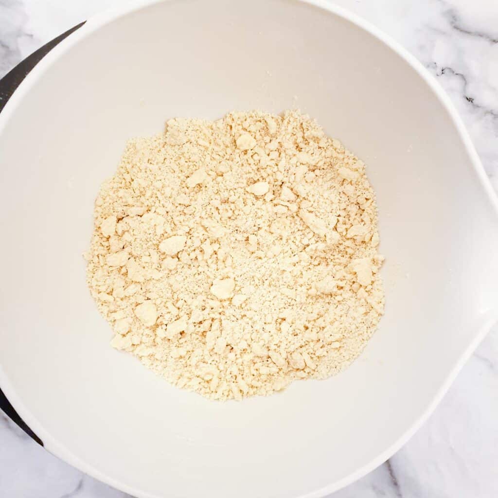 Flour and butter rubbed together to form fine breadcrumbs in a white mixing bowl.