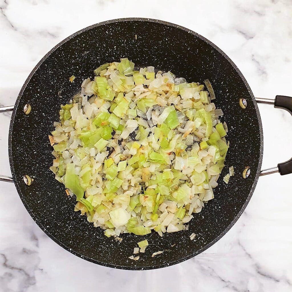 Chopped onions and leeks being softened in a frying pan.