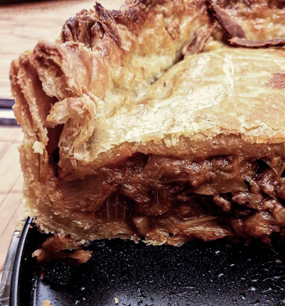 A close up of the inside of the raised beef and onion pie showing the flaky texture of the pastry.