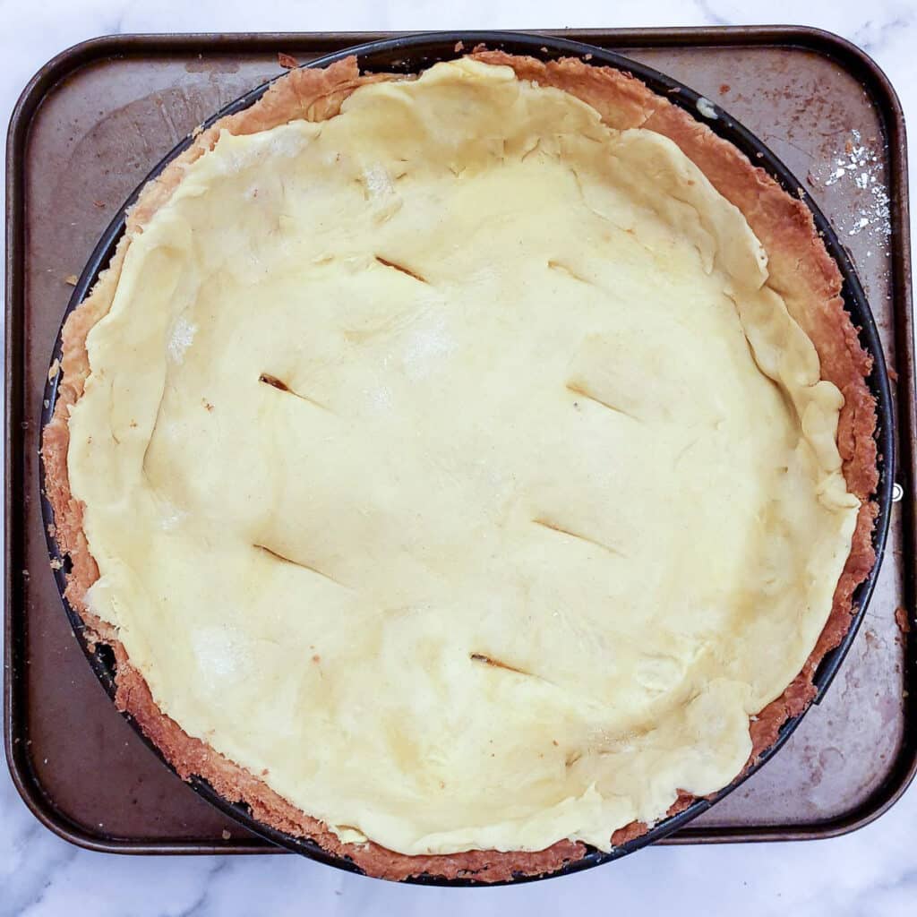 A circular piece of uncooked pastry on top of a beef and onion pie.