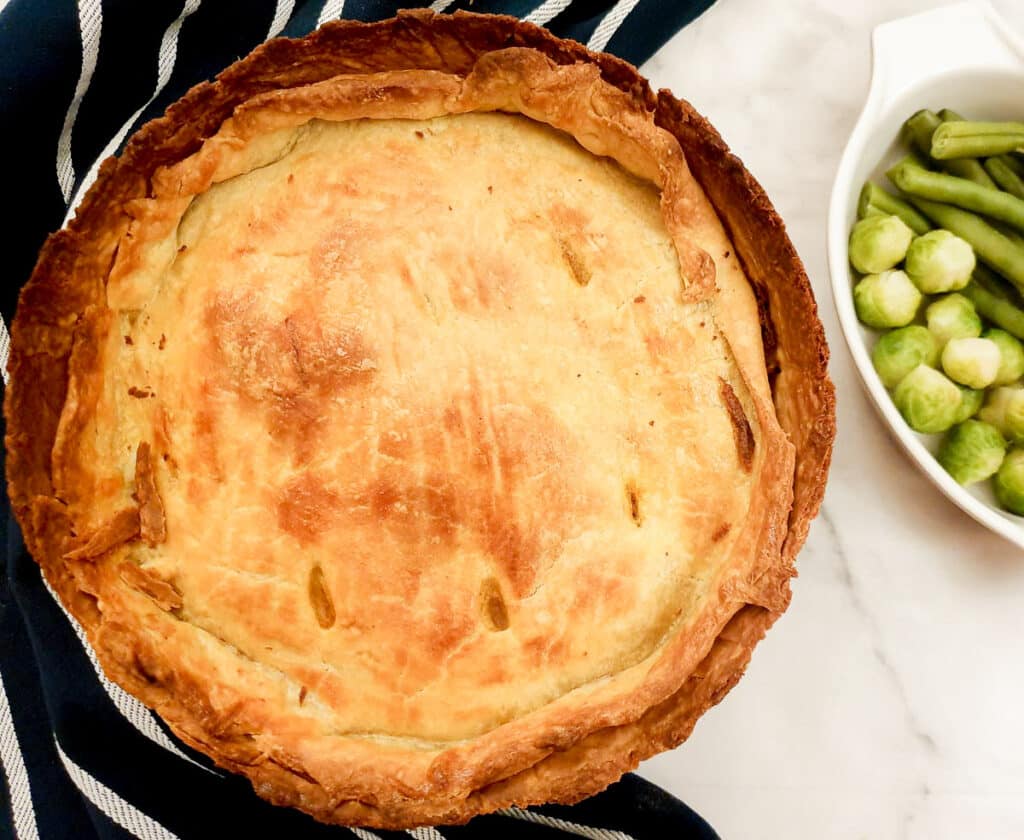 Overhead shot of a raised beef and onion pie next to a dish of vegetables.