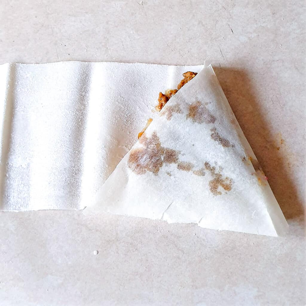 Samosa pastry being folded again into a triangle shape.