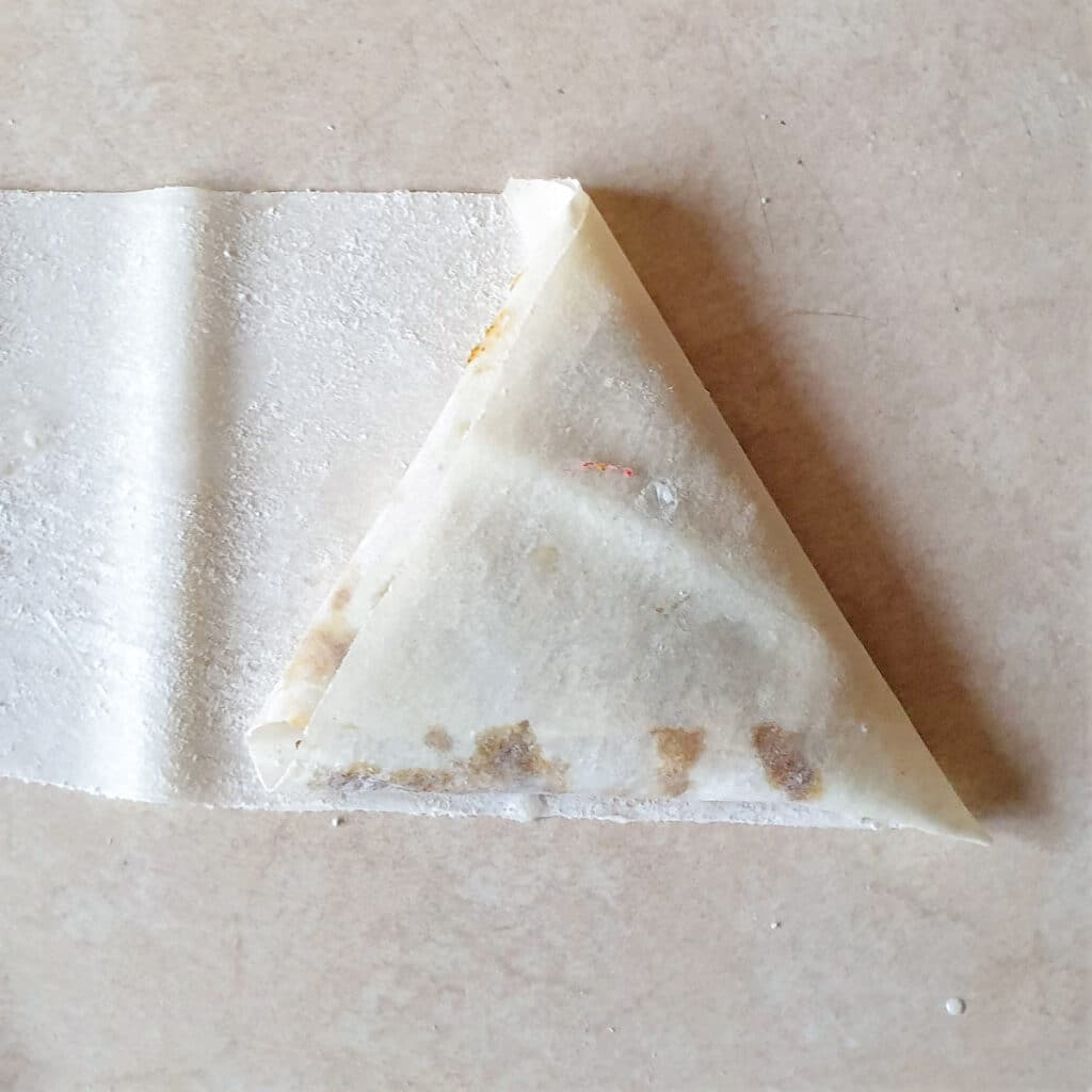 The final fold of a triangular samosa made with phyllo pastry.