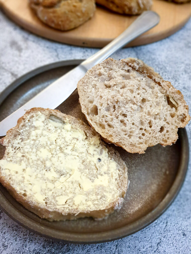 A seeded breadroll cut in half and spread with butter.