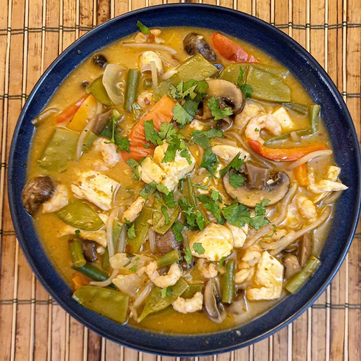 Thai red curry seafood in a blue serving dish garnished with chopped coriander.