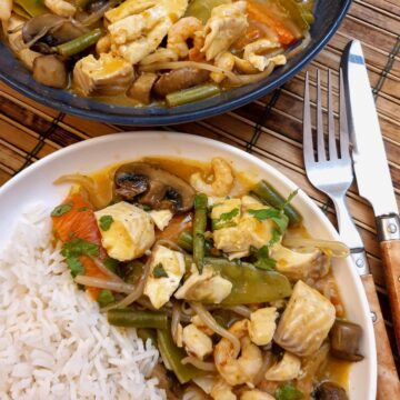 A plate of Thai red curry seafoon on a white plate with a helping of jasmine rice.