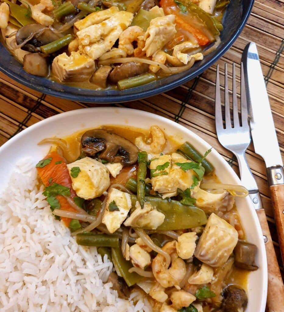 A plate of Thai red curry seafoon on a white plate with a helping of jasmine rice.