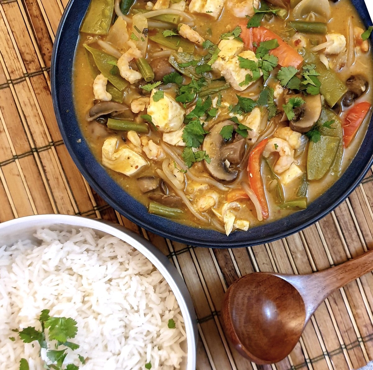 Overhead shot of a dish of Thai red curry seafood next to a bowl of jasmine rice.