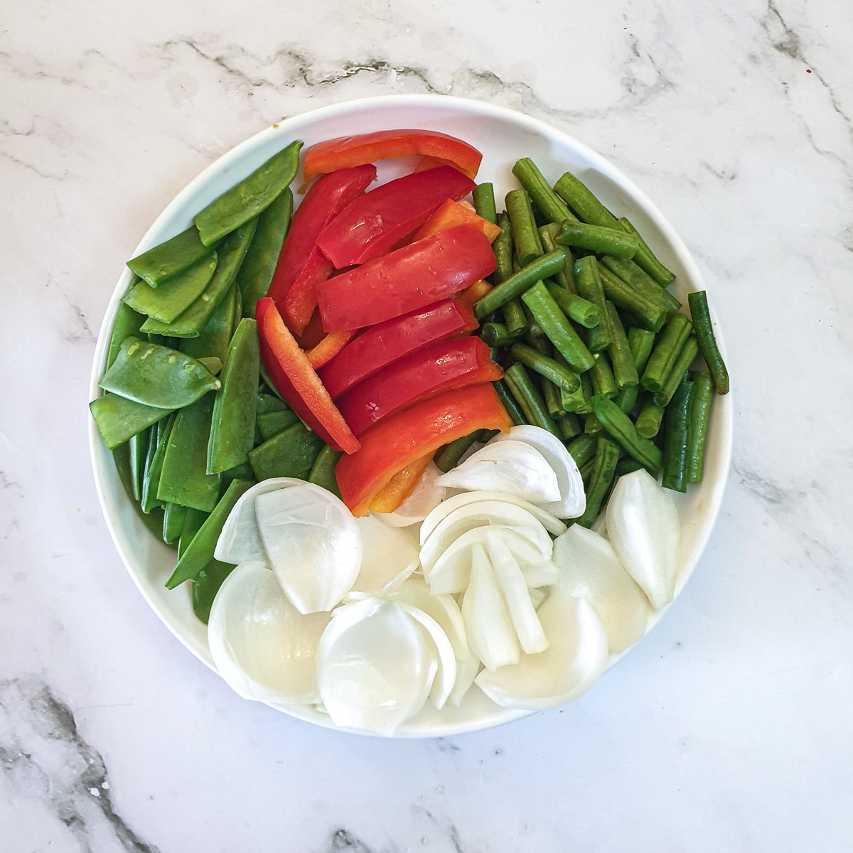 A dish of raw chopped red pepper, green beans, mangetout and onions.