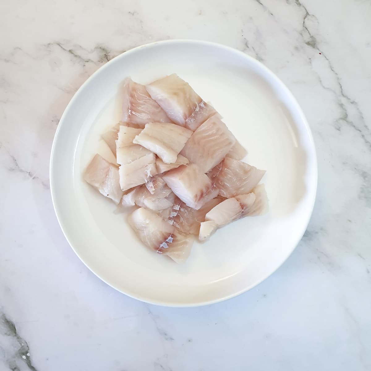 A plate of raw fish cut into chunks.